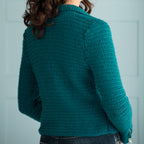 Teal crochet sweater worn by a person against a light blue background