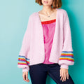 Person wearing a pink cardigan with colorful cuffs against a blue background