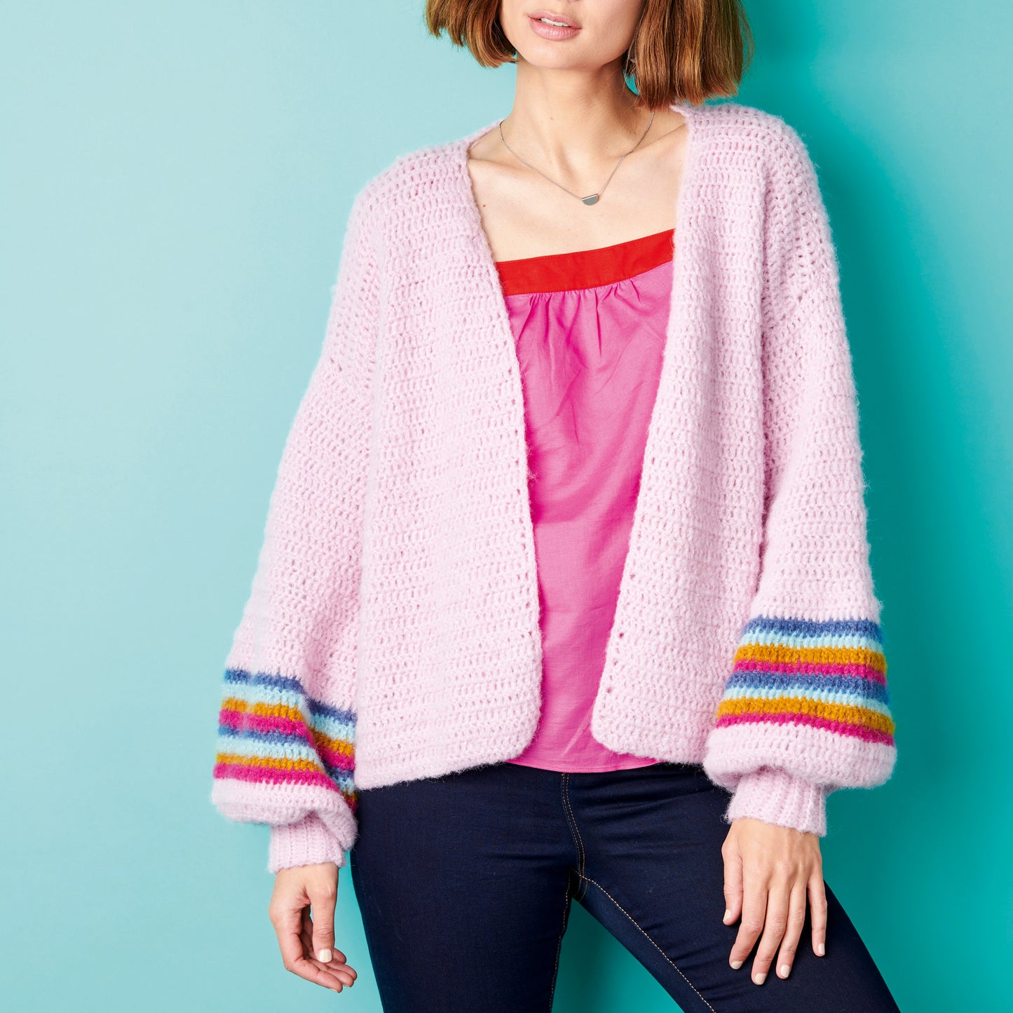 Person wearing a pink cardigan with colorful cuffs against a blue background