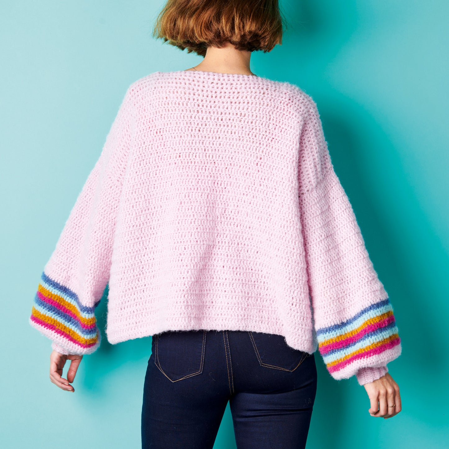 Person wearing a pink crochet sweater with colorful sleeves against a blue background