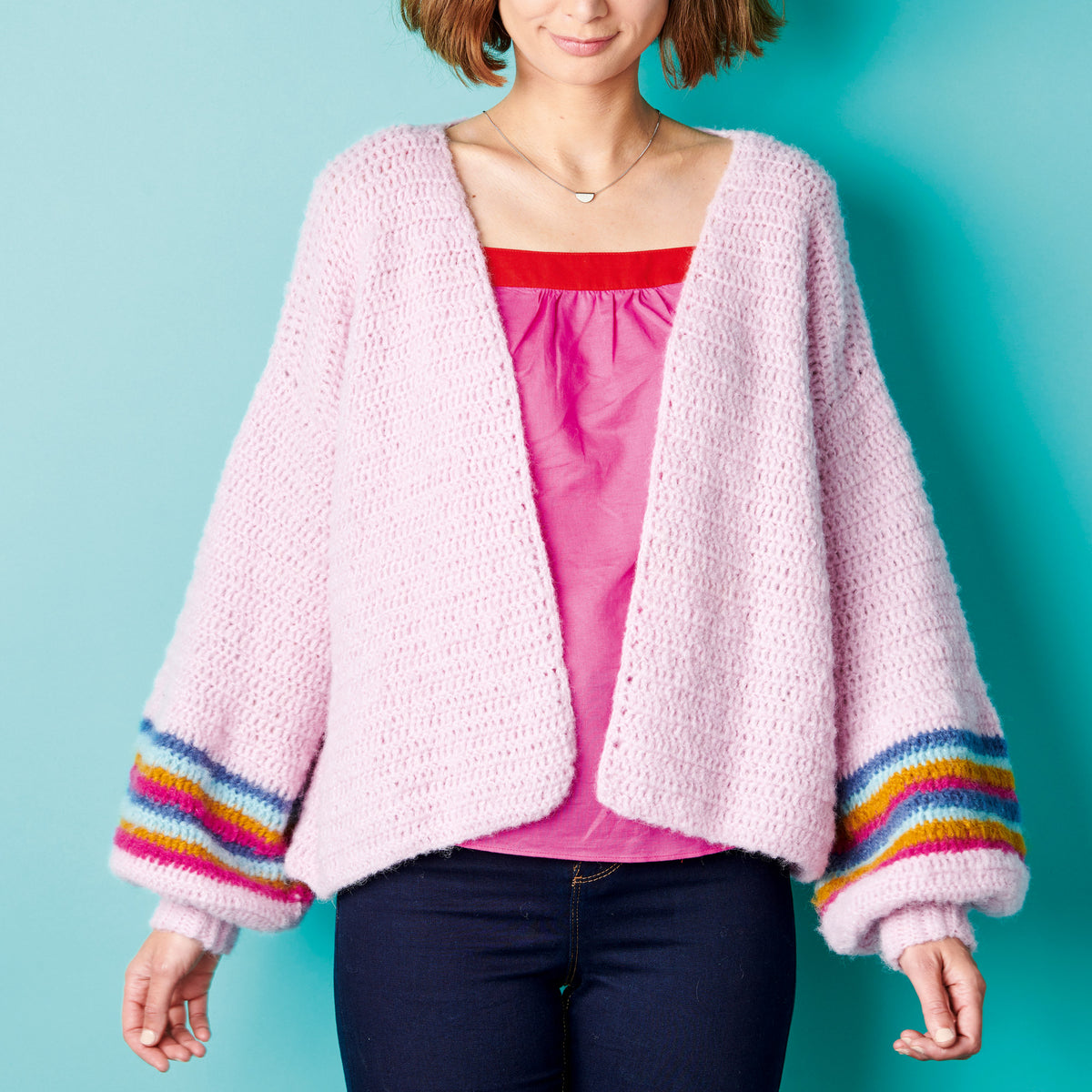 Woman wearing a pink cardigan with colorful sleeves against a teal background