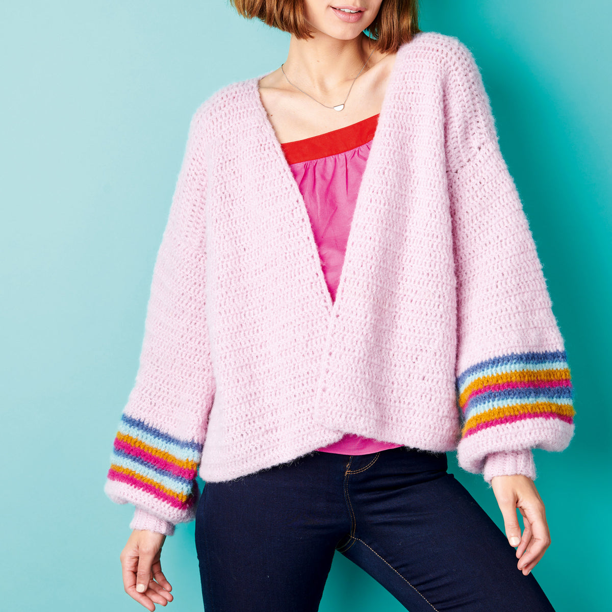 Woman wearing a pink cardigan with colorful cuffs against a teal background
