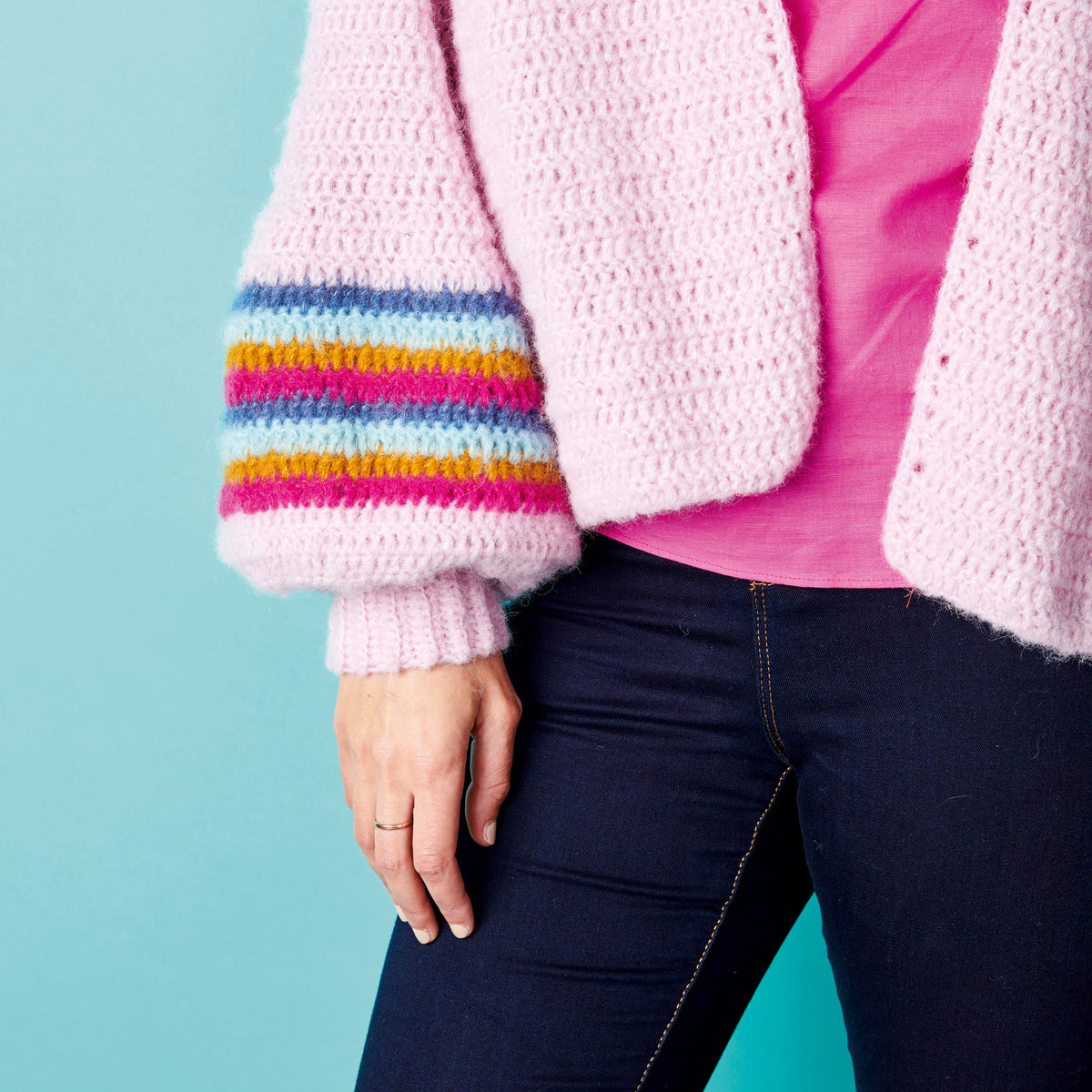 Person wearing a pink crochet cardigan with colorful sleeves against a blue background