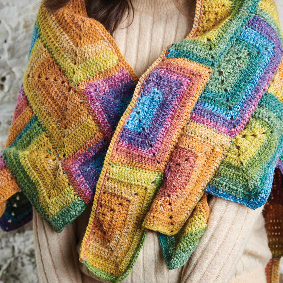 Colorful crocheted shawl with geometric pattern draped over a person wearing a beige sweater.