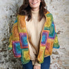 Woman wearing a colorful crocheted cardigan against a stone wall.