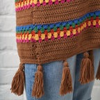 Brown crochet sweater with colorful trim and tassels on a light gray background