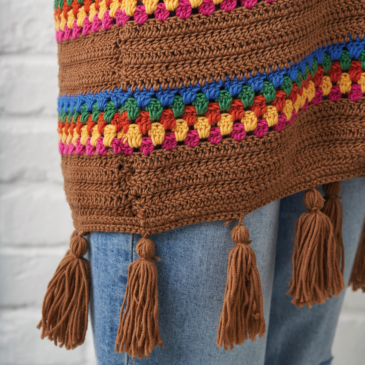 Brown crochet sweater with colorful trim and tassels on a light gray background