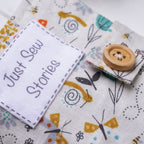 Fabric with embroidered designs and a wooden button, featuring the text 'Just Sew Stories'.