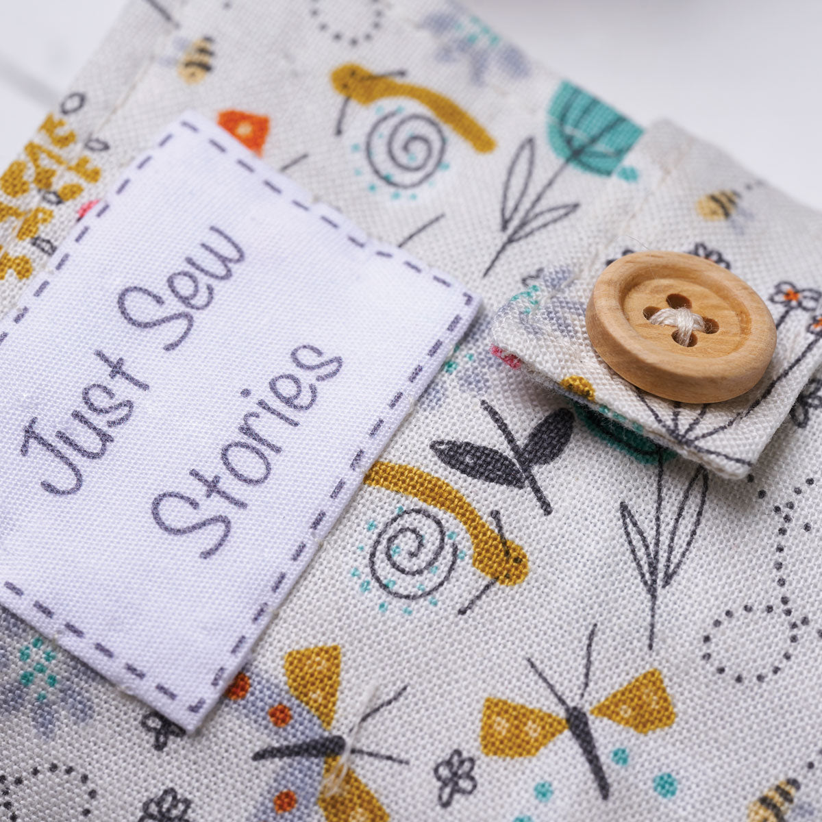 Fabric with embroidered designs and a wooden button, featuring the text 'Just Sew Stories'.