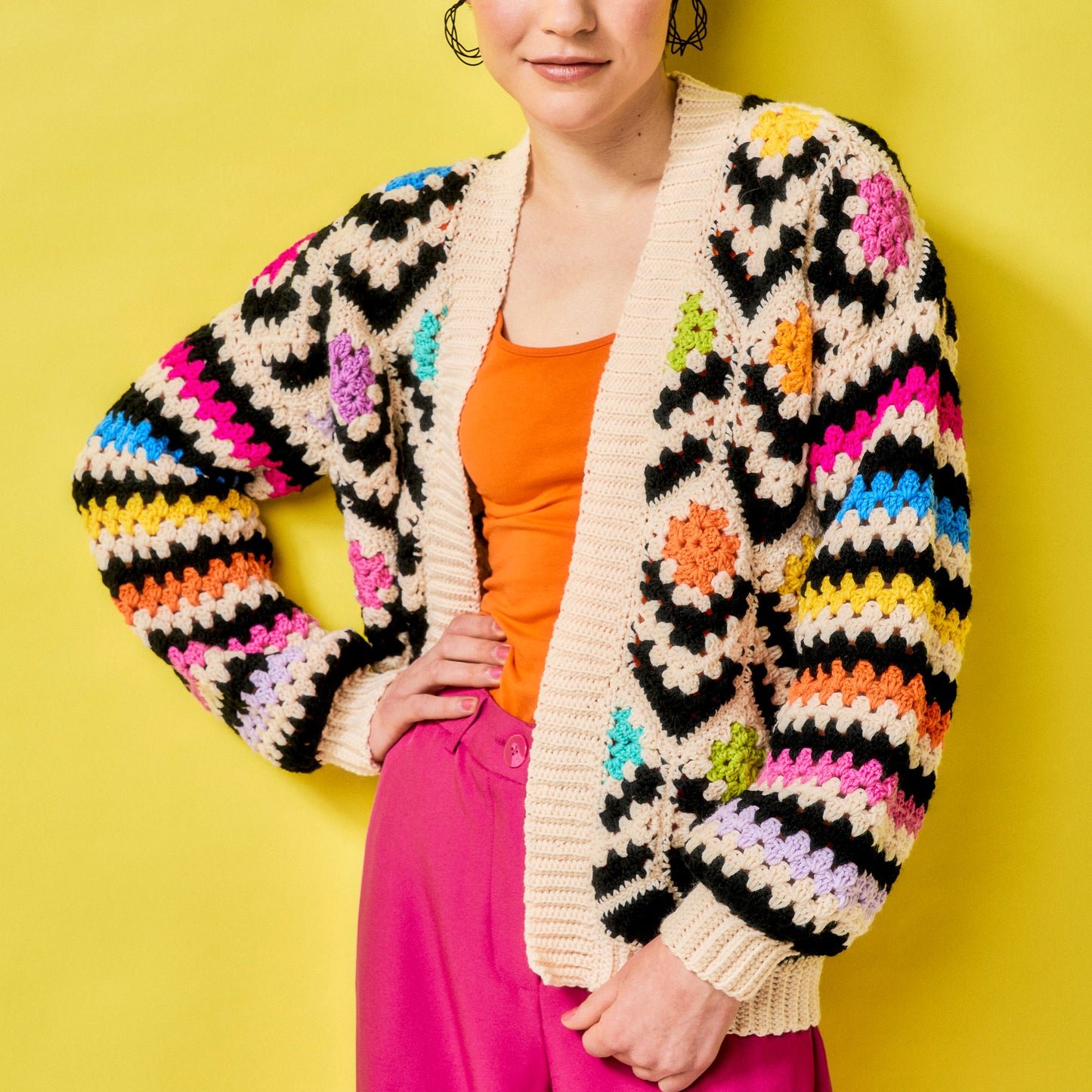 Person wearing a colorful crochet cardigan against a yellow background