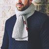 A person wearing a gray brioche stitch scarf with red buttons.