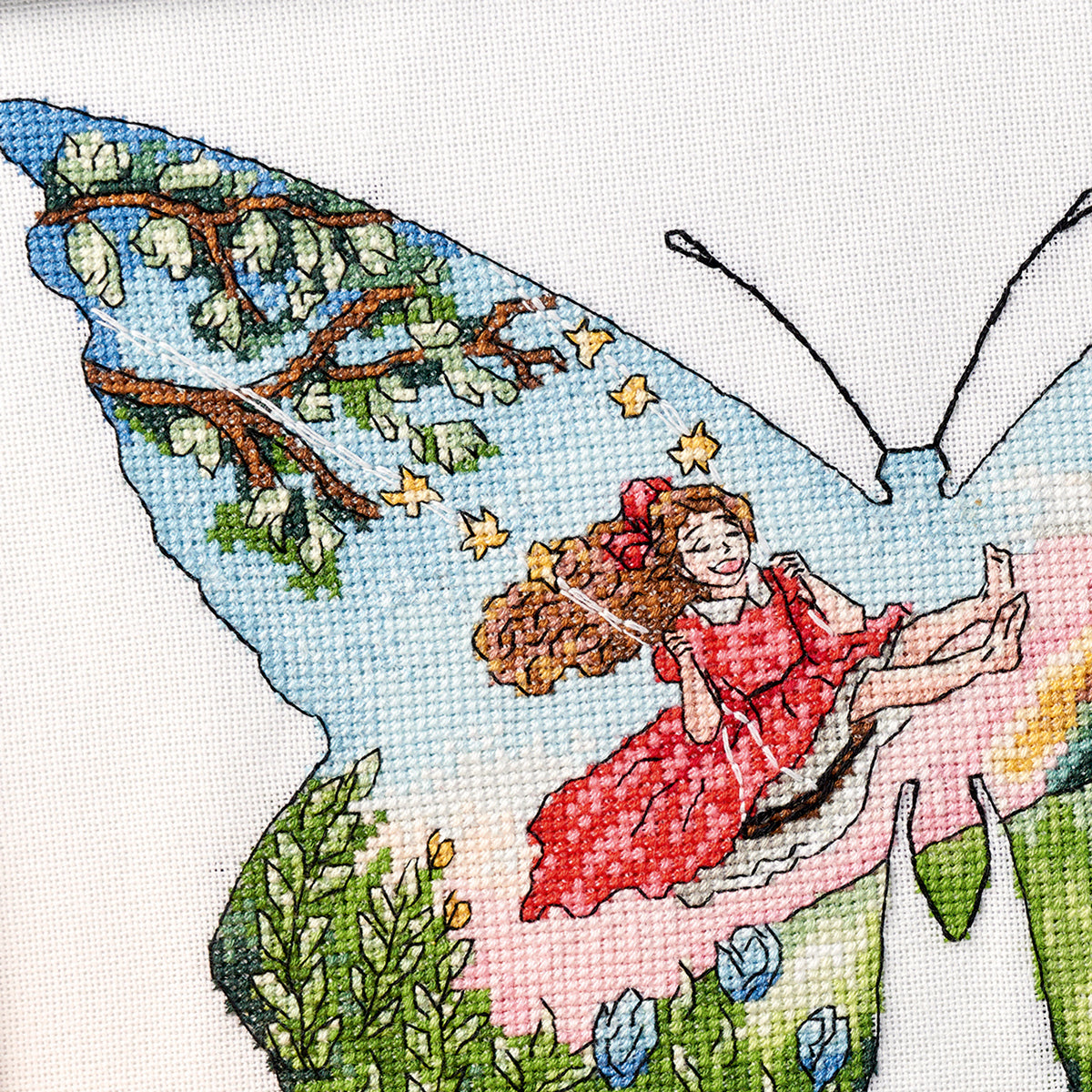 Cross-stitched design of a fairy in a red dress sitting on a butterfly wing with a tree and flowers in the background.