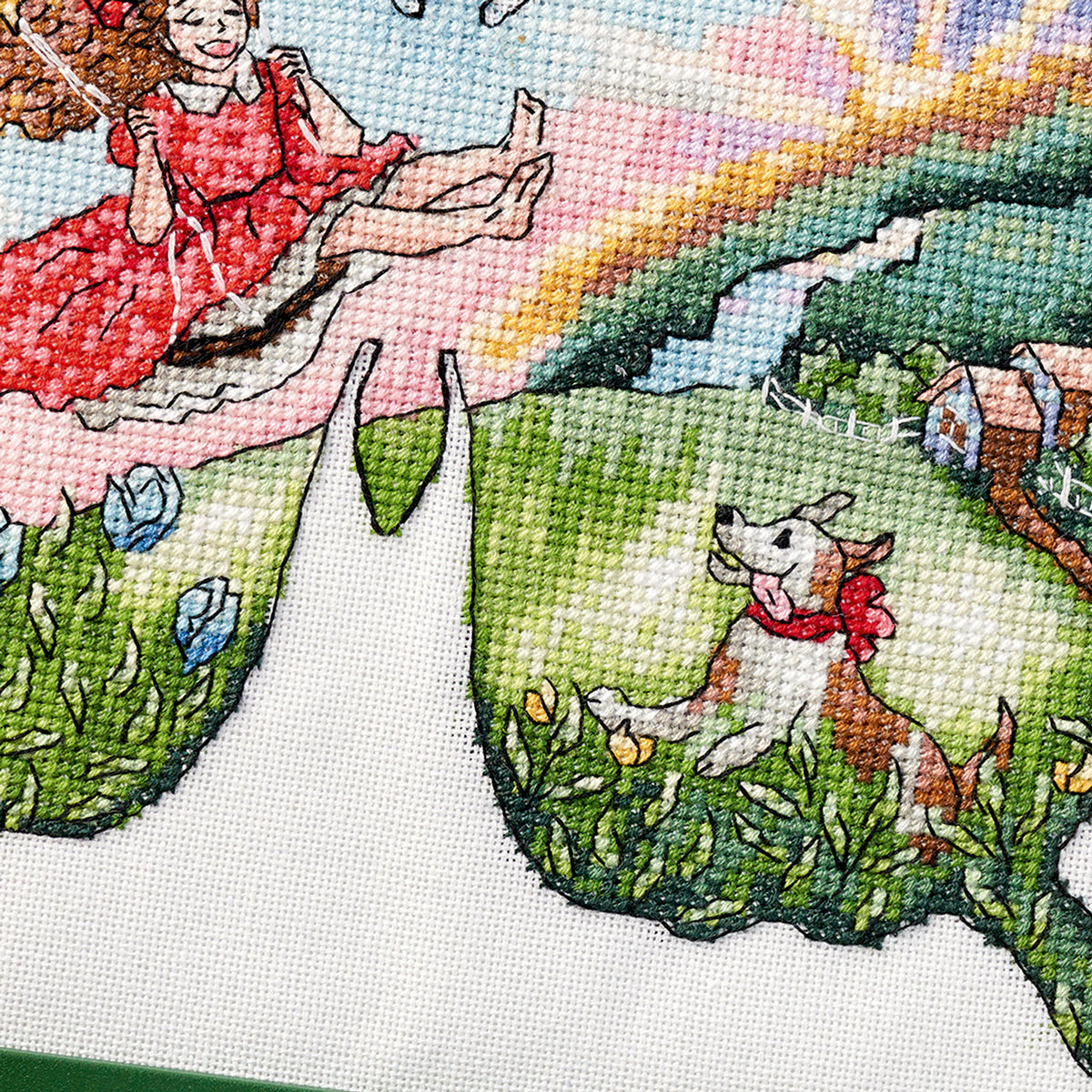 Cross-stitched scene with a girl on a swing and a dog in a field