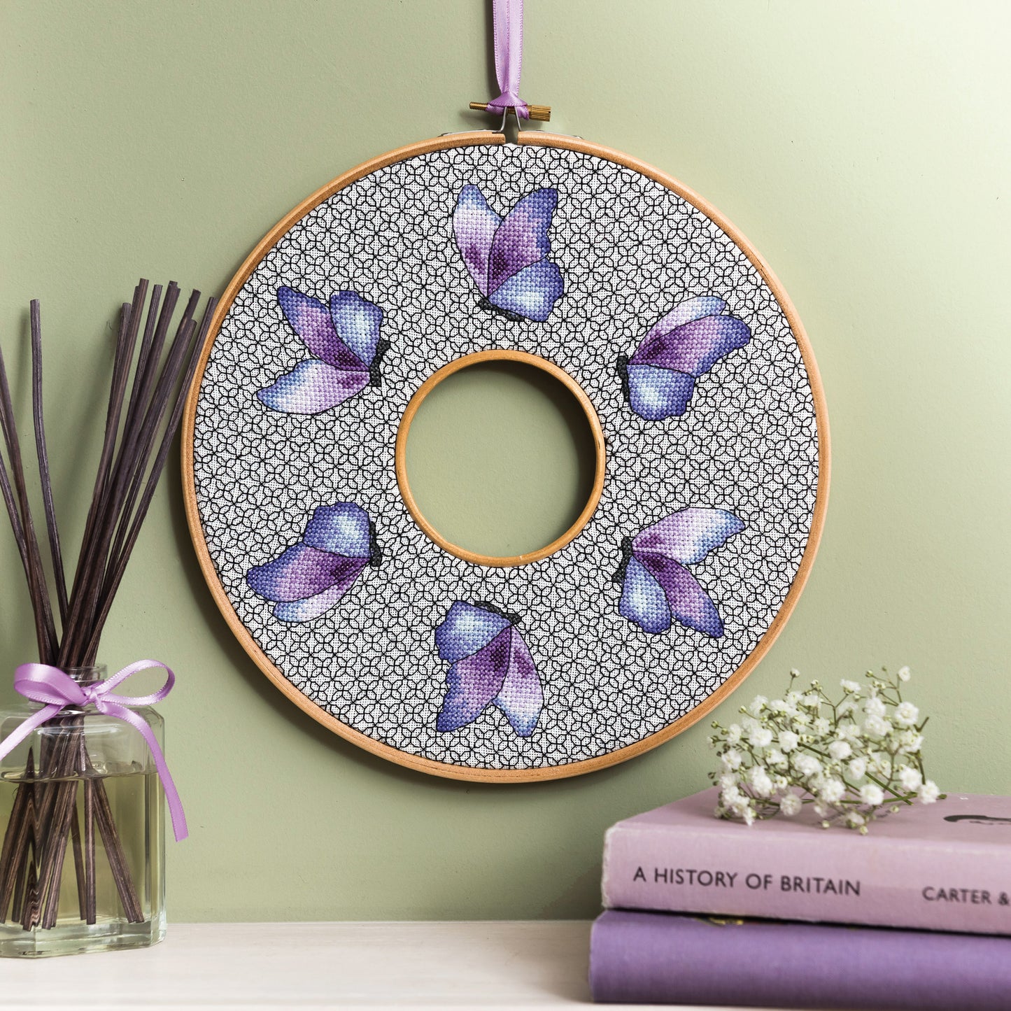 Embroidery hoop with butterfly design on a green wall, books, and flowers in the foreground.