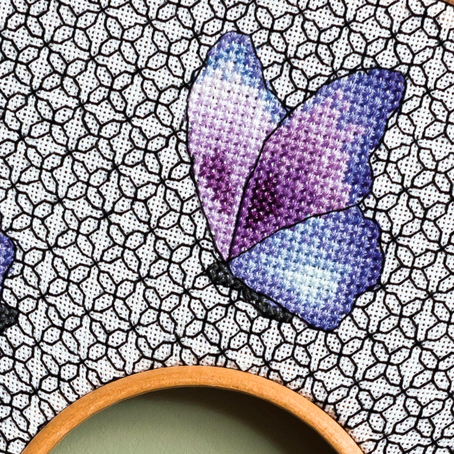 Cross-stitched butterfly design on fabric with a wooden coaster in the foreground