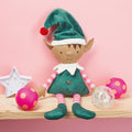 Elf doll with green hat and striped shirt on a pink background