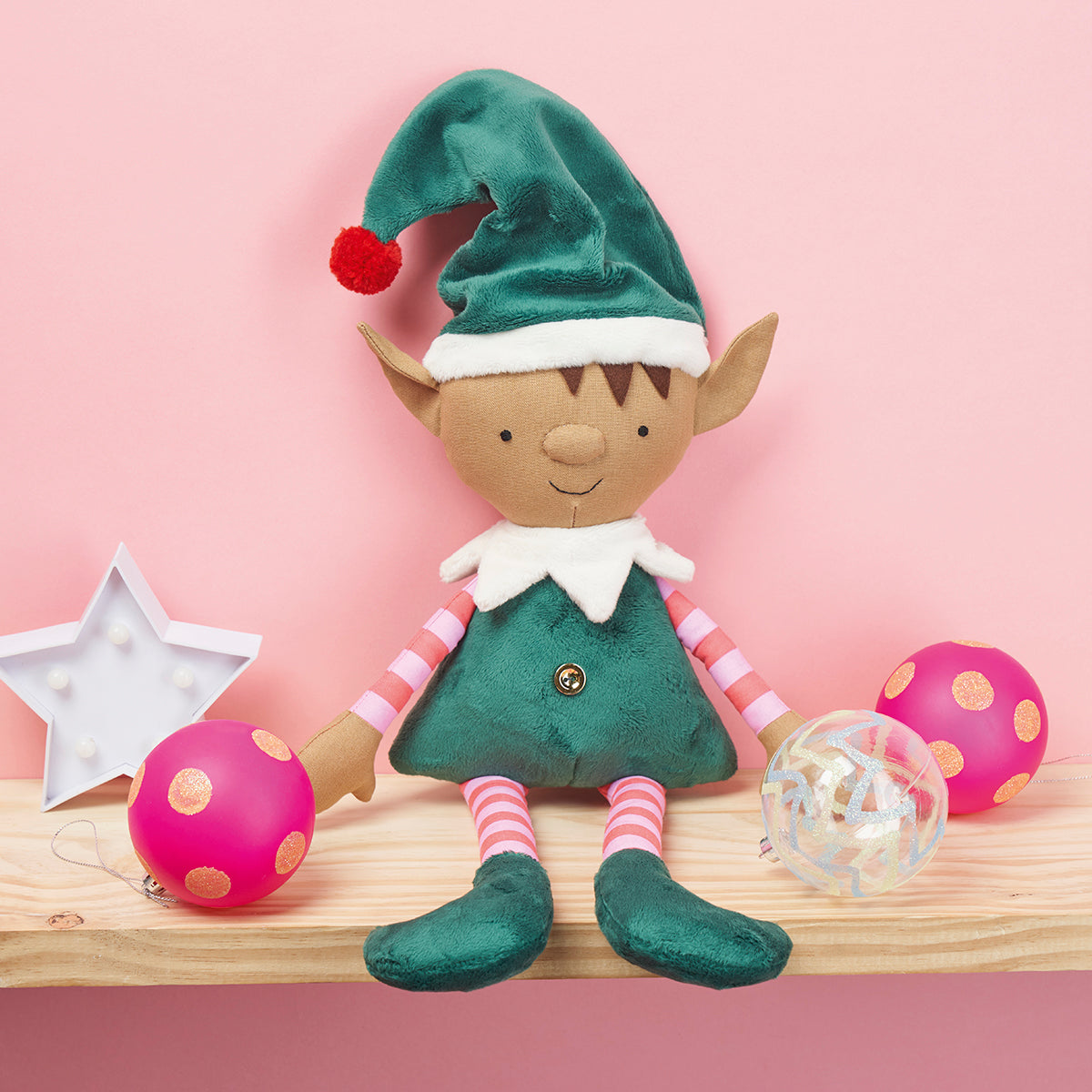 Elf doll with green hat and striped shirt on a pink background