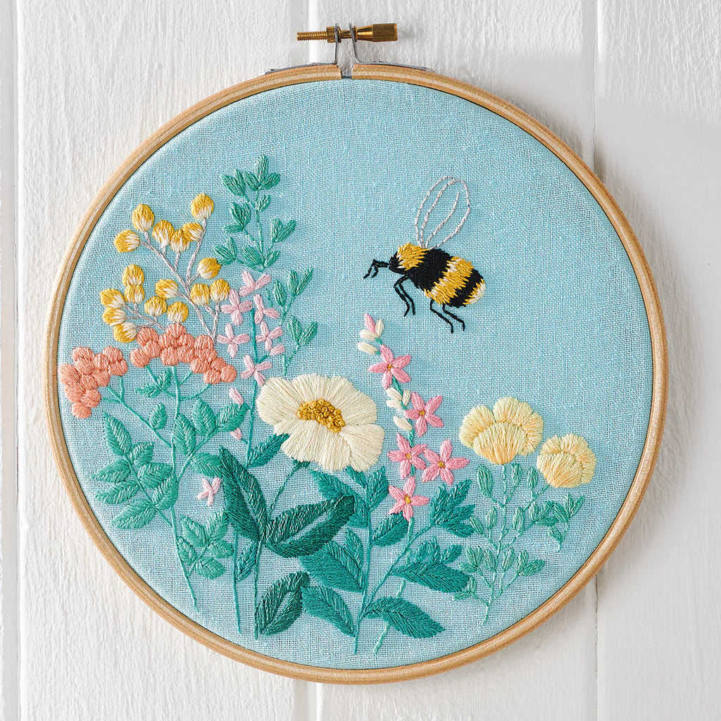 Embroidery hoop with floral and bee design on a light blue background
