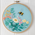 Embroidery hoop with floral and bee design on a light blue background