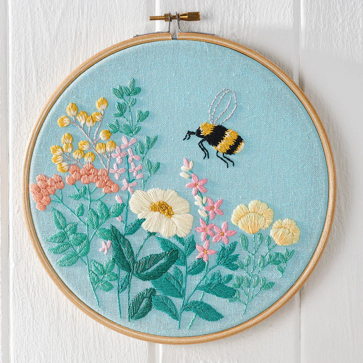 Embroidery hoop with floral and bee design on a light blue background