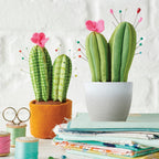 Cactus-shaped pincushions with pink flowers on a stack of fabric and scissors.
