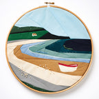 Embroidery hoop with a landscape scene featuring boats and mountains on a white background