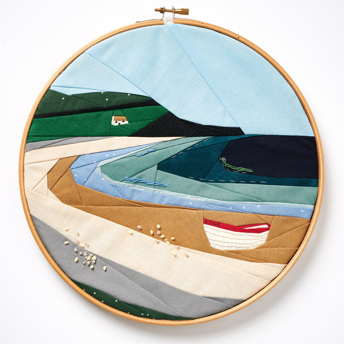 Embroidery hoop with a landscape scene featuring boats and mountains on a white background