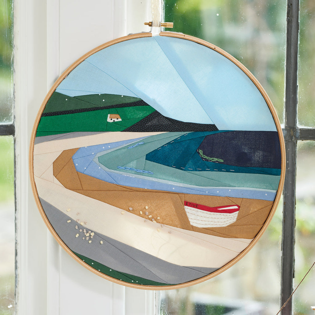 Embroidery hoop with a scenic landscape design featuring a house, boat, and mountains.