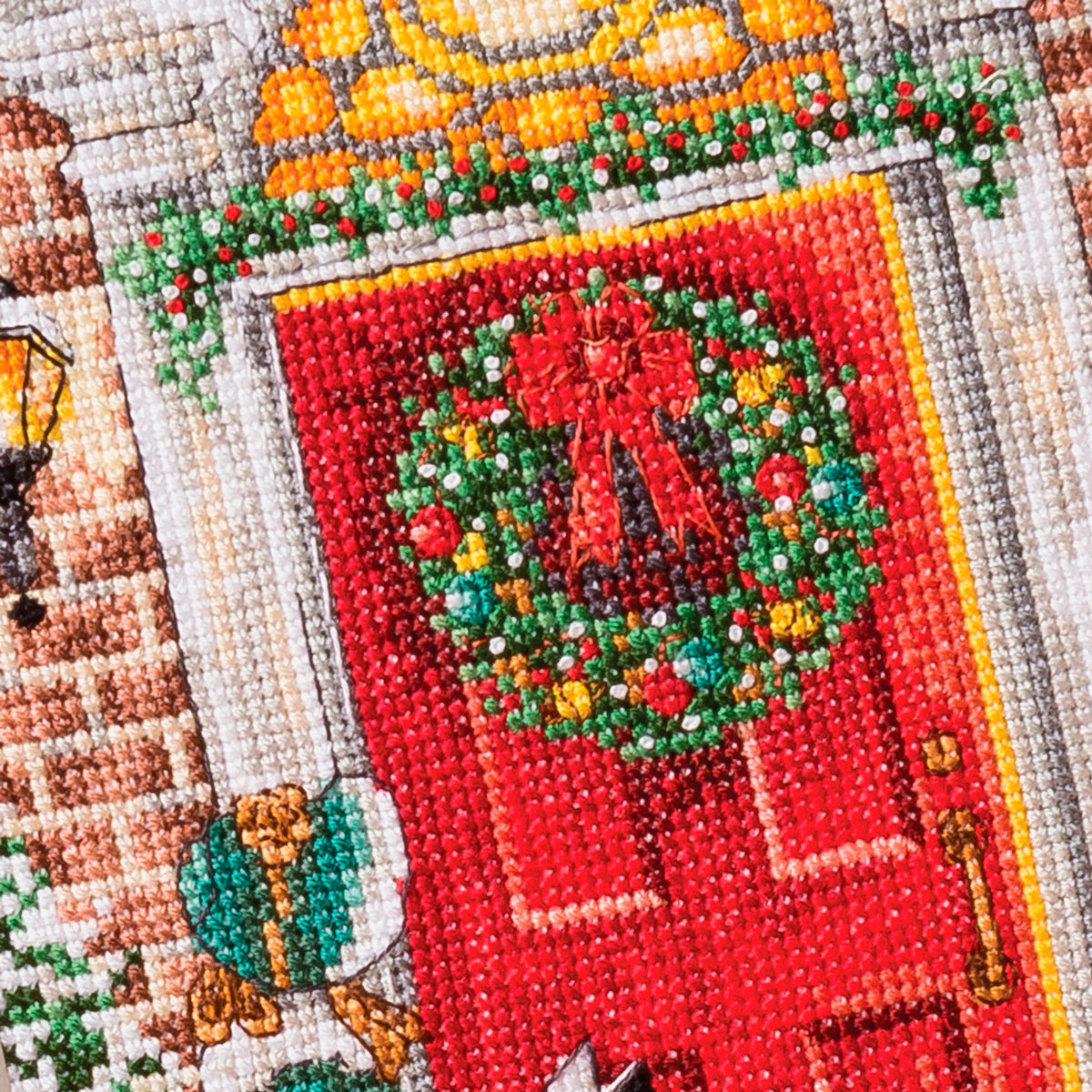 Cross-stitched Christmas wreath design on fabric with a red background and greenery.