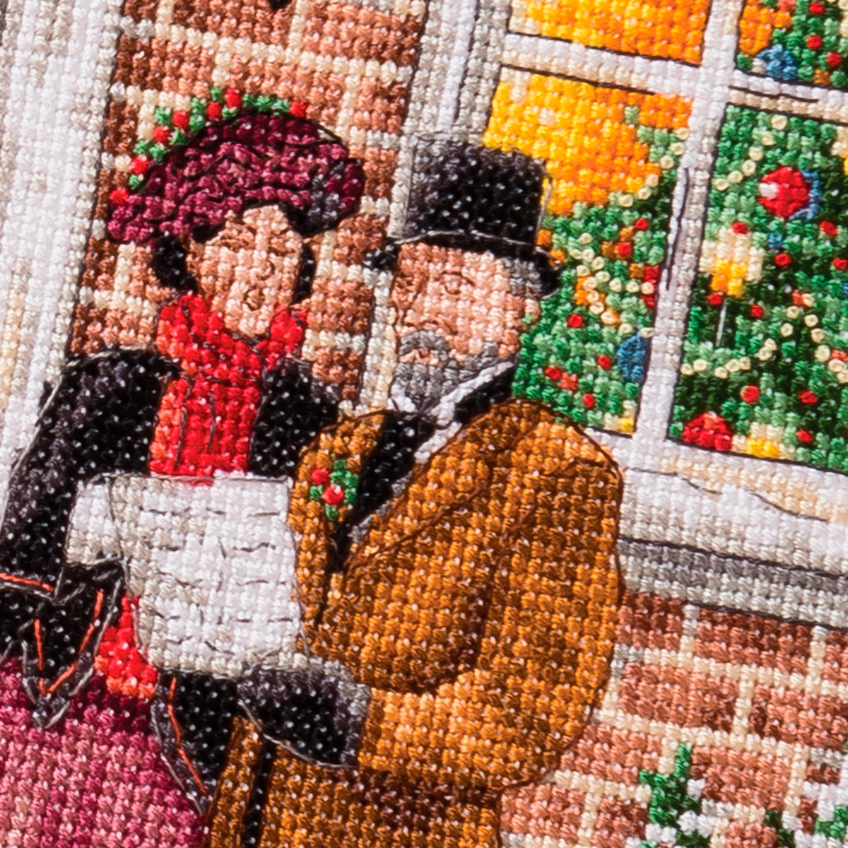 Close-up of a cross stitch depicting two people in winter clothing with a window display in the background.