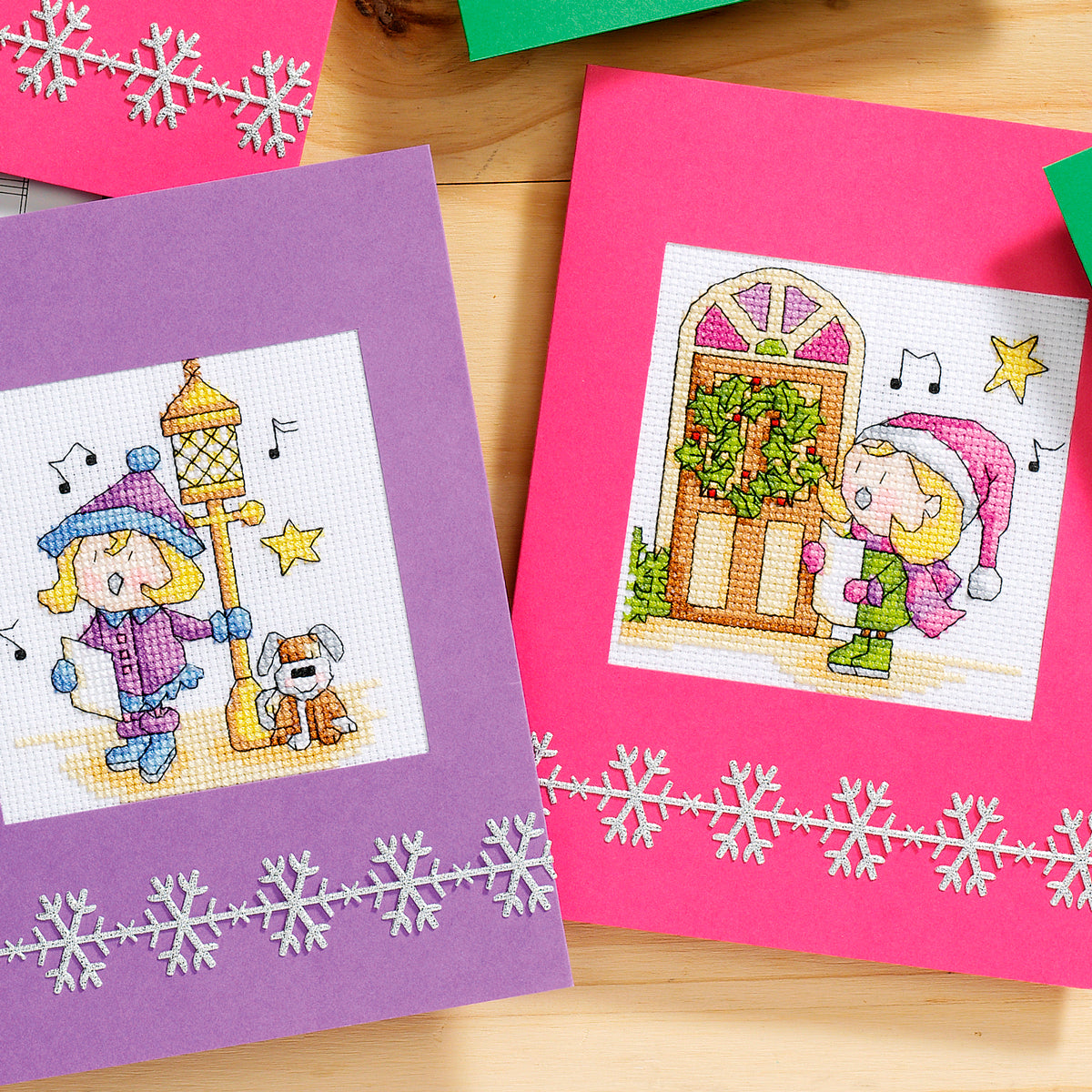 Two cross-stitched cards on a wooden surface with snowflake designs.