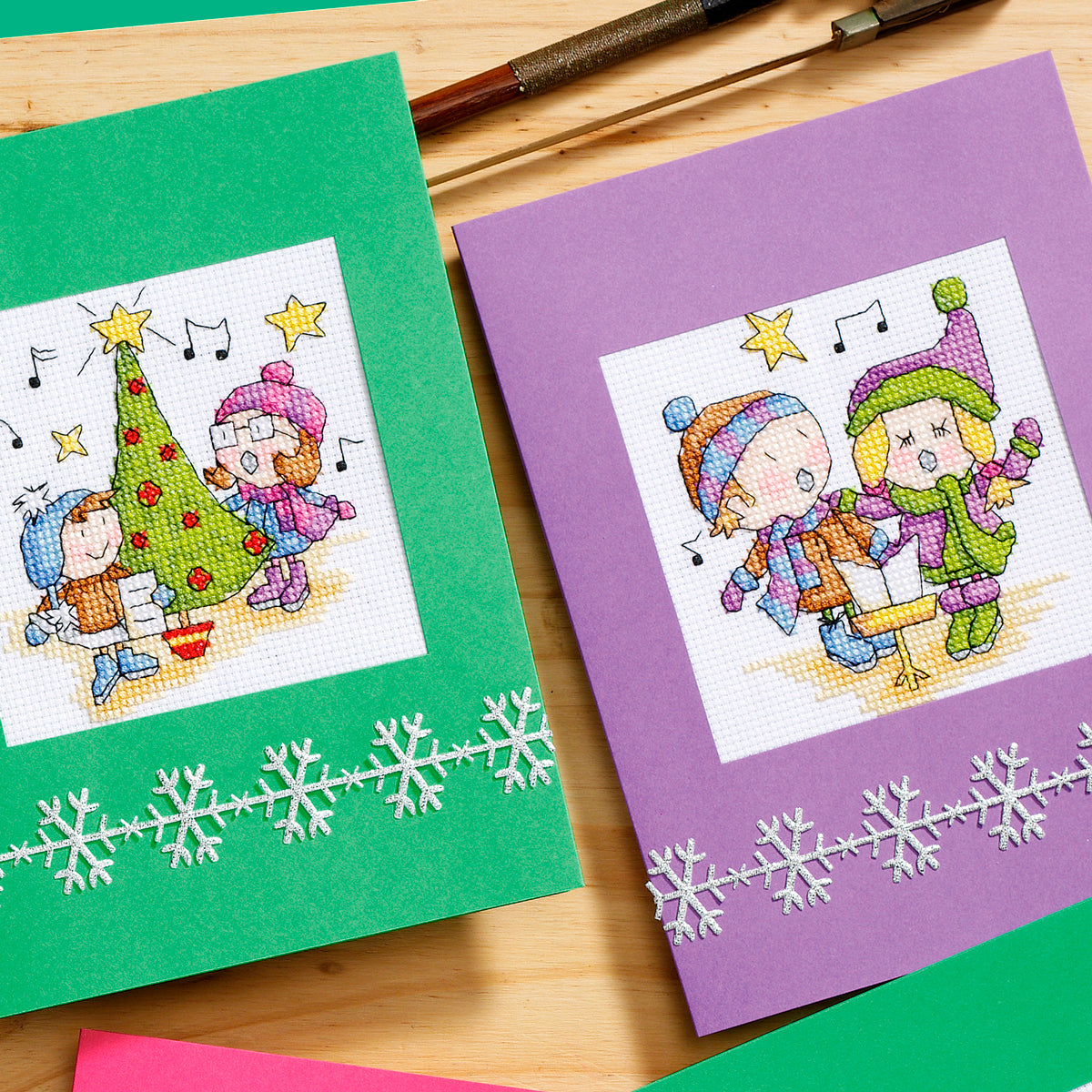 Two cross-stitched cards on a wooden surface with snowflake designs.