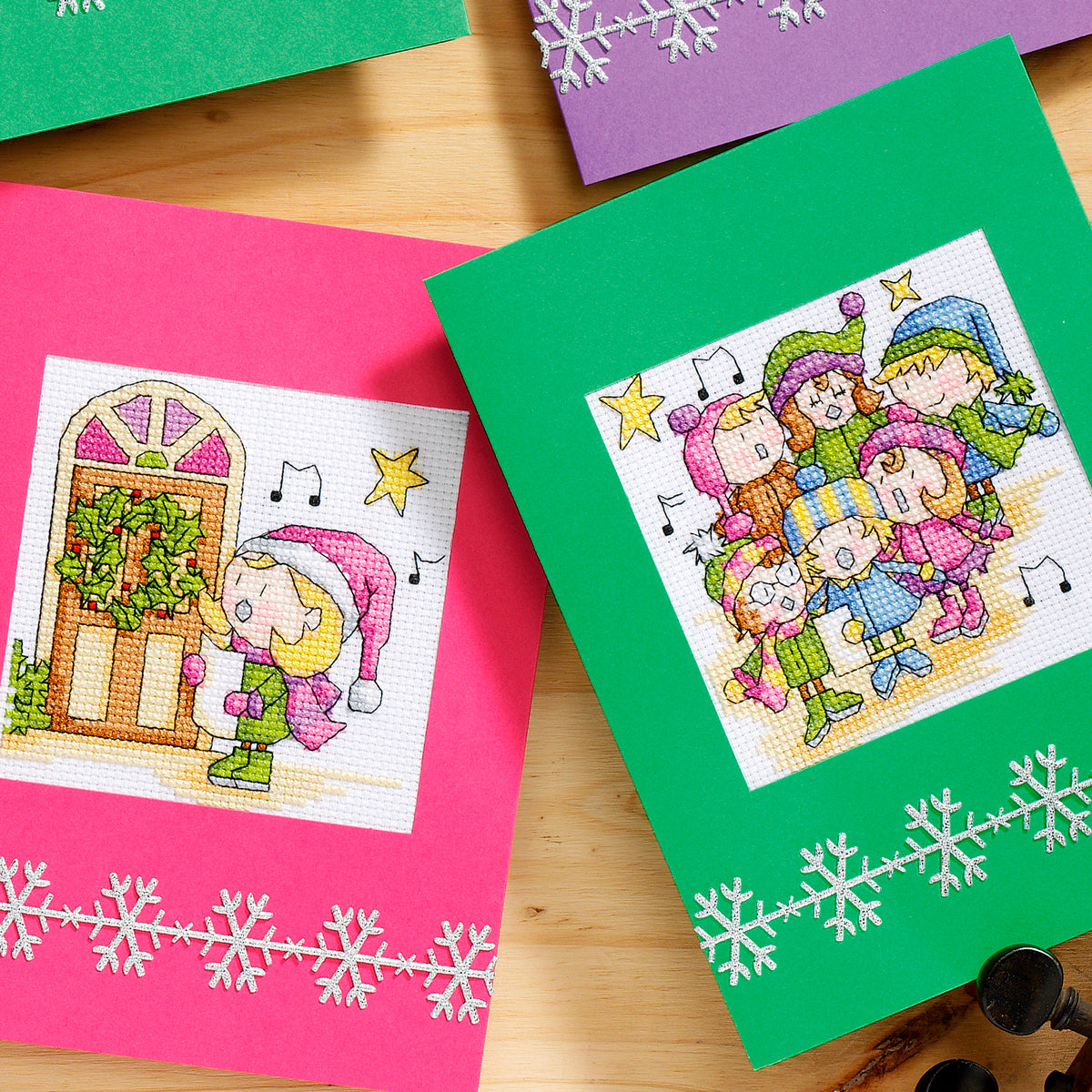 Colorful Christmas cards with cross-stitch designs on a wooden surface