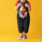 Child wearing a colorful geometric-patterned bib overalls on a yellow background