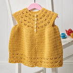 Yellow crocheted dress on a pink hanger against a white background