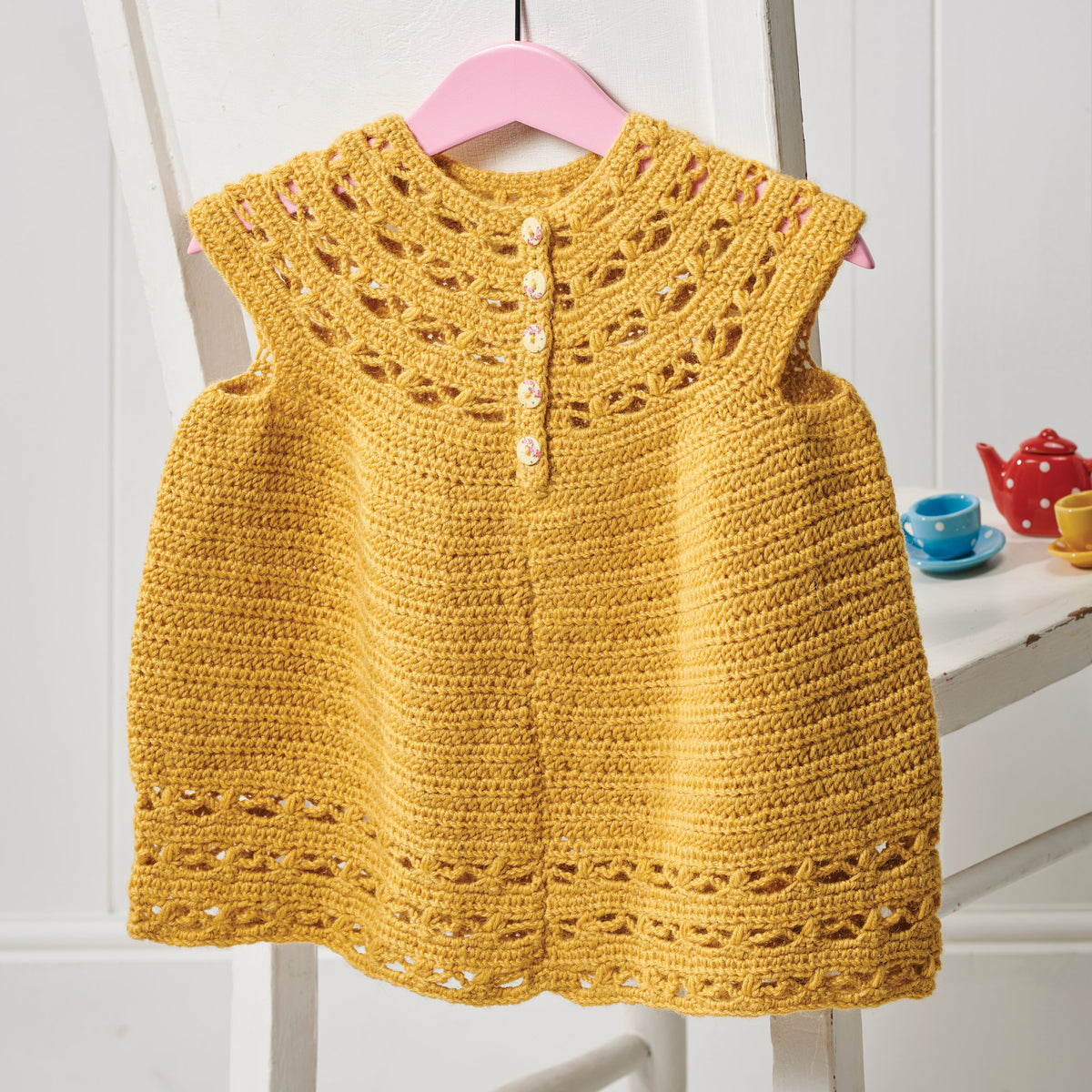 Yellow crocheted dress on a pink hanger against a white background