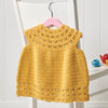 Yellow crocheted dress on a white chair with a pink hanger.