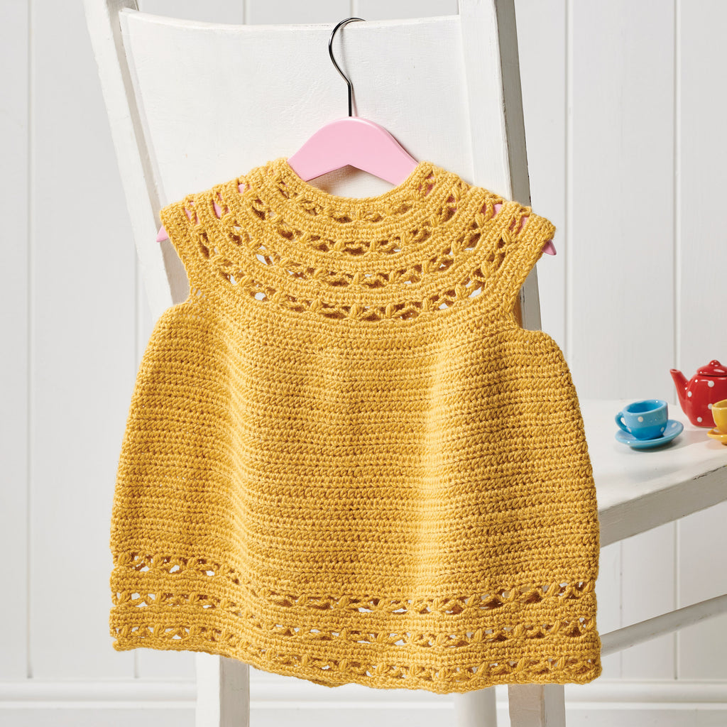 Yellow crocheted dress on a white chair with a pink hanger.