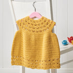 Yellow crocheted dress on a white chair with a pink hanger.