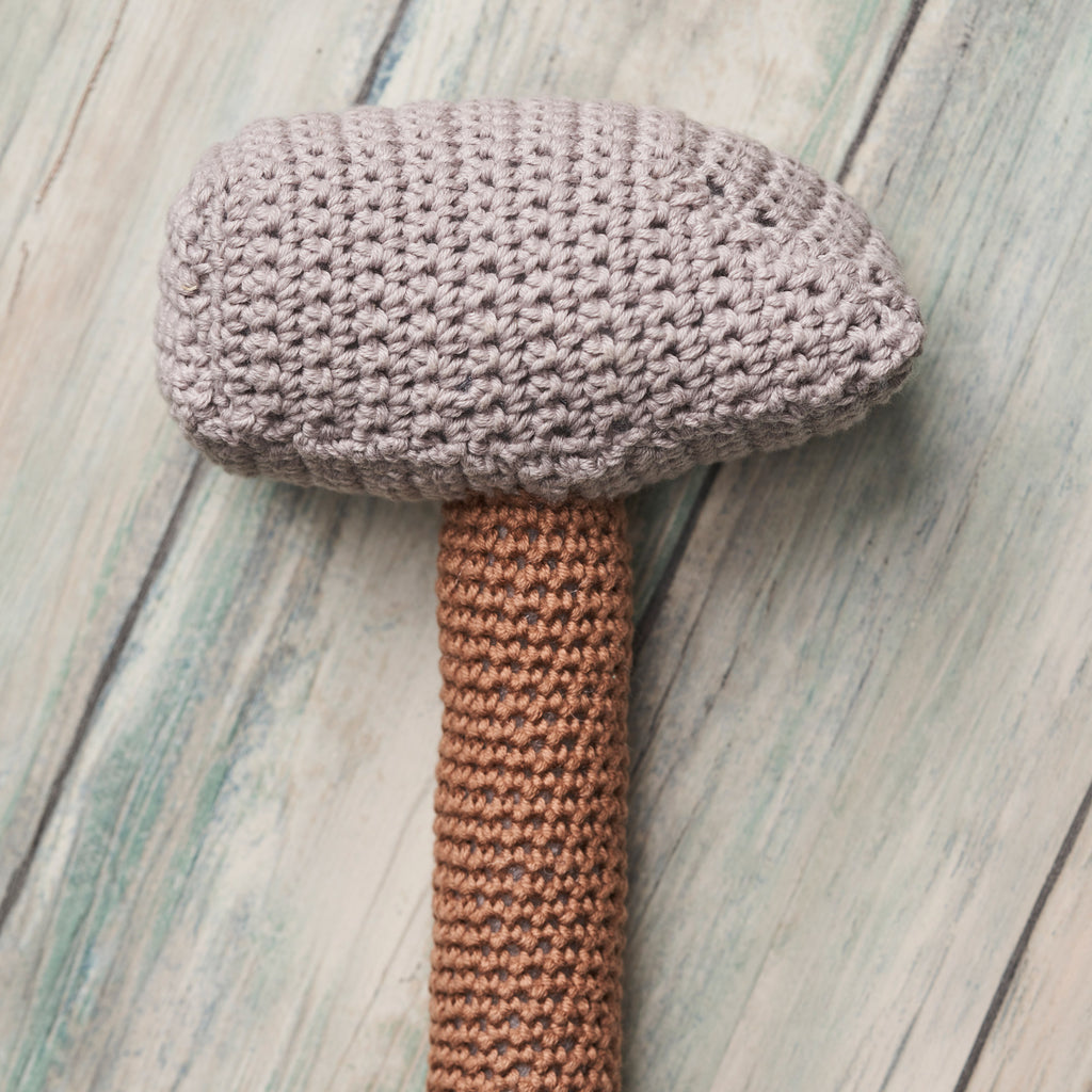 Crocheted toy hammer with a brown handle and gray head on a wooden surface