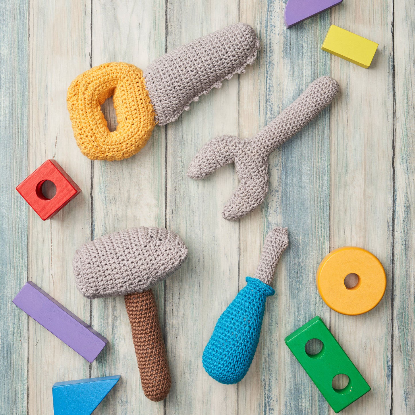 Crocheted toy tools and colorful blocks on a wooden surface
