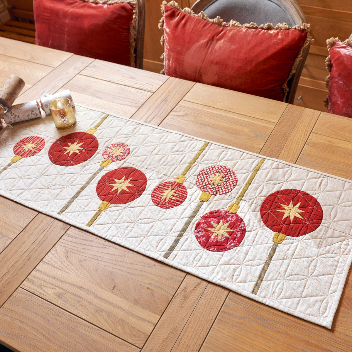 Quilted table runner with red and gold floral design on a wooden table.
