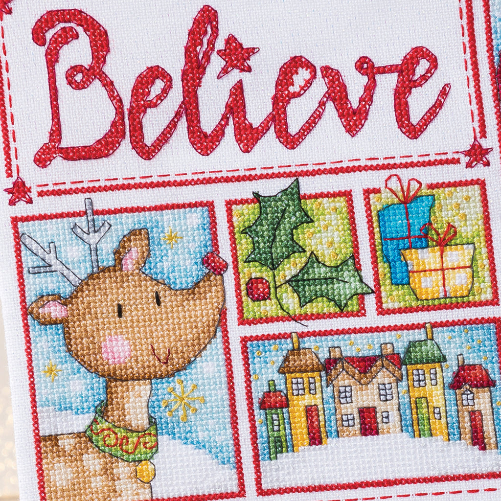 Cross-stitched design with a reindeer, holly, presents, and houses, featuring the word 'Believe'.