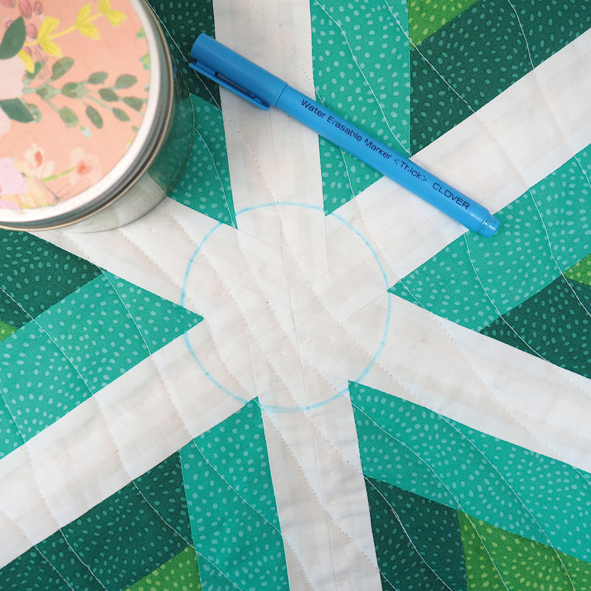 Quilt with geometric pattern and blue marking pen on a green surface