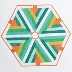 Hexagonal quilt with green, orange, and white pattern on a white background