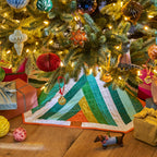 Decorated Christmas tree with ornaments, lights, and a quilt on a wooden floor.
