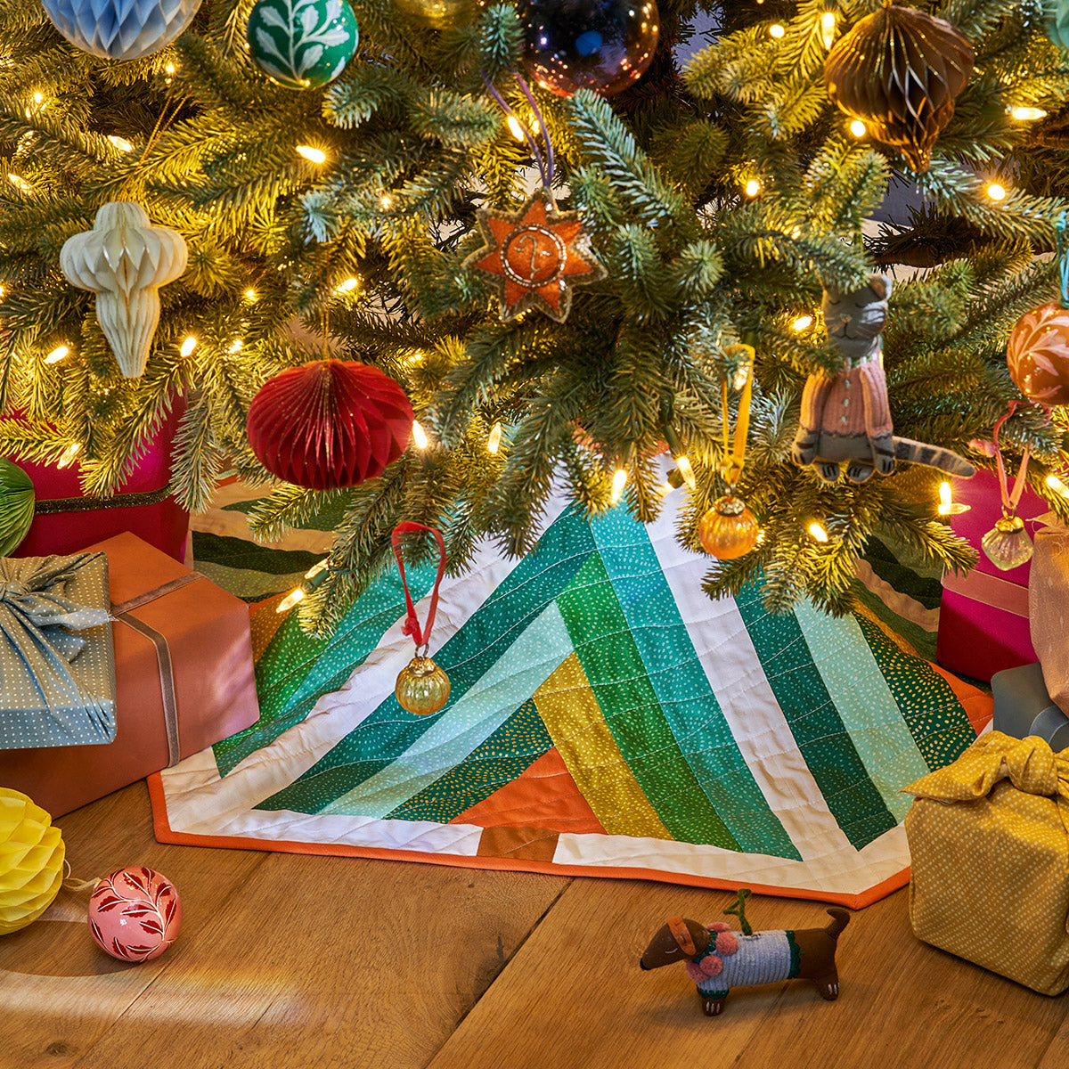 Decorated Christmas tree with ornaments, lights, and a quilt on a wooden floor.