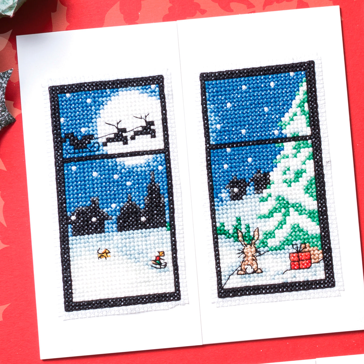 Cross-stitched design of a snowy scene with a window view on a red background