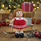 Knitted doll in a red dress with a Christmas tree and presents in the background
