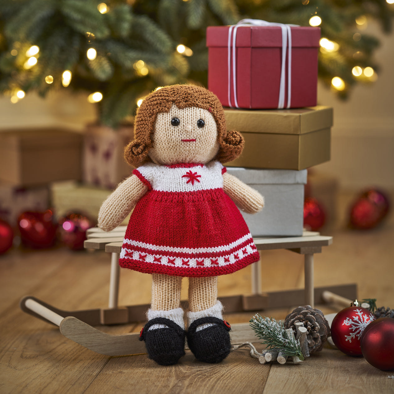 Knitted doll in a red dress with a Christmas tree and presents in the background
